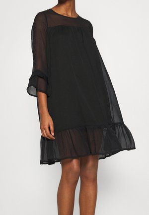 Vestido de gasa negra de corte suelto, con cuerpo transparente, mangas tres cuartos y bajo con volantes, con escote alto y textura suave.