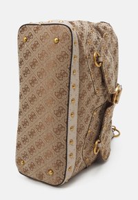 Borsa designer a motivo marrone con borchie dorate, anelli e fibbie, mostrata in una vista laterale inclinata su uno sfondo bianco.
