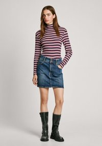 Top de rayas de manga larga en varios colores, combinado con una falda de mezclilla azul. La modelo lleva botas negras hasta la rodilla. Texturas suaves y diseño ajustado.