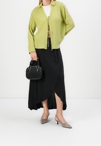 Chemise boutonnière texturée vert clair, jupe portefeuille noire, escarpins gris à bout pointu, et un petit sac à main noir avec un motif matelassé.