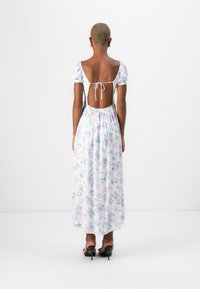 Rochie maxi cu mâneci bufante, model floral în culori pastelate, design cu spatele deschis și închidere cu fundă, talie elastică. Sandale cu toc negre.