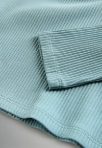 Tissu côtelé bleu clair avec coutures visibles, montrant une manche longue pliée et une partie de l'ourlet du vêtement.