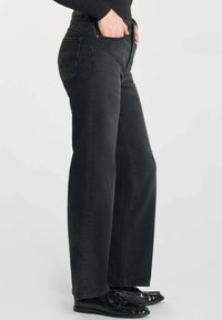 Zwarte wijde spijkerbroek van denim, met een hoge taille, twee achterzakken en een rechte pasvorm. Gecombineerd met glanzende zwarte schoenen.