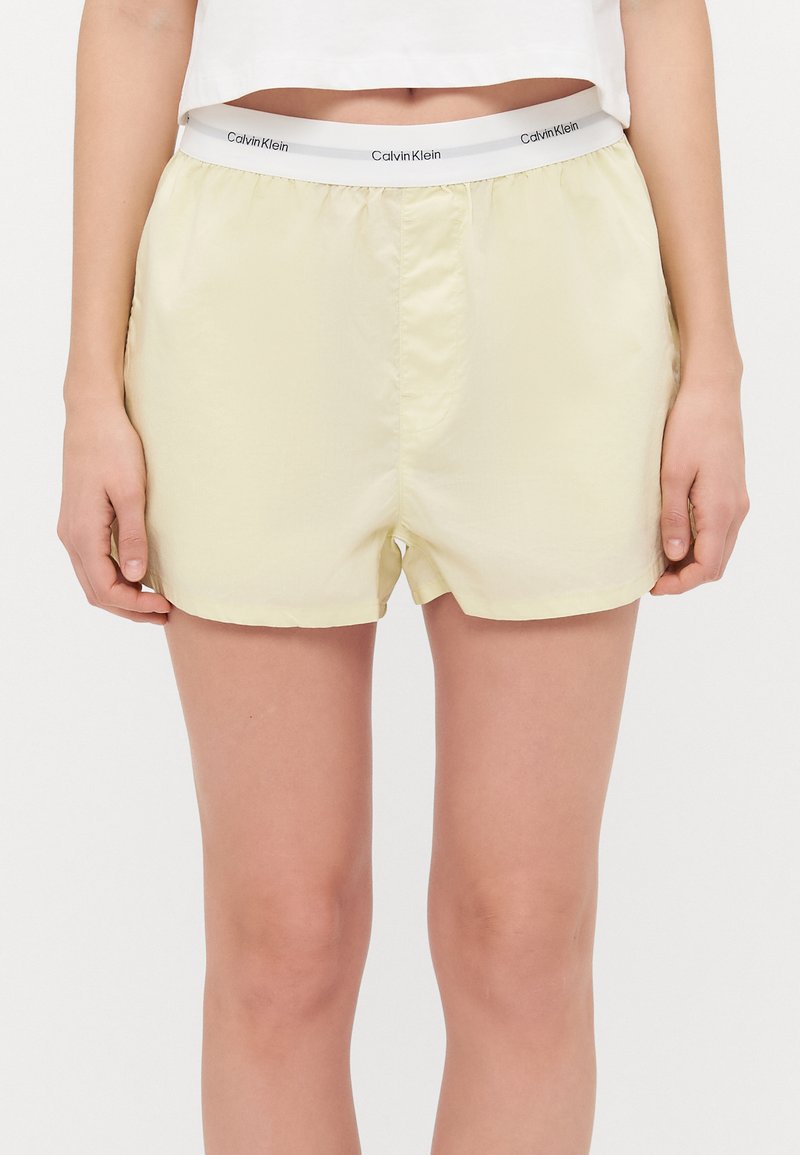 Lichtgele shorts gemaakt van gladde stof met een elastische tailleband waarop het Calvin Klein-logo in het grijs staat. De zoom eindigt halverwege de dij.