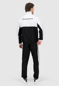Zwart-witte trainingsjack met logo, elastische boorden en bijpassende broek. Kenmerkt zich door strepen aan de zijkanten, gemaakt van lichtgewicht stof.