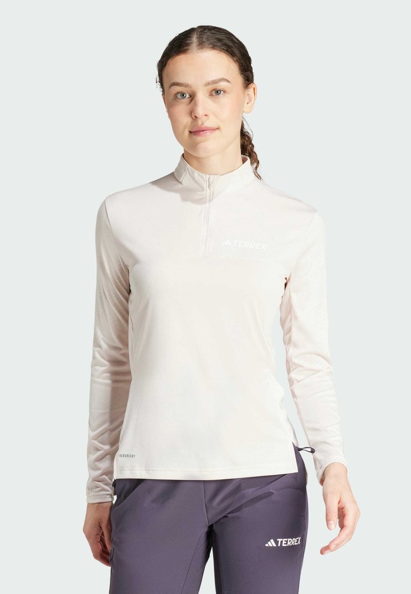 Langarm, lichtroze sporttop met een kwartrits en hoge kraag; voorzien van een reflecterend logo en een gladde, rekbare stof.