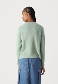 Minzgrüner, gerippter Pullover mit Raglanärmeln, kombiniert mit einem Jeansrock. Die Textur ist weich, der Schnitt lässig und der Ausschnitt schlicht.