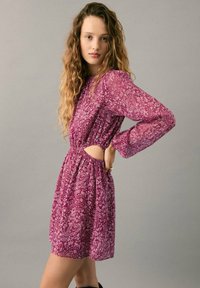Robe courte violette à motifs cachemire avec manches longues, côtés découpés, taille élastique et coupe décontractée. Présente des motifs floraux sur toute la surface.