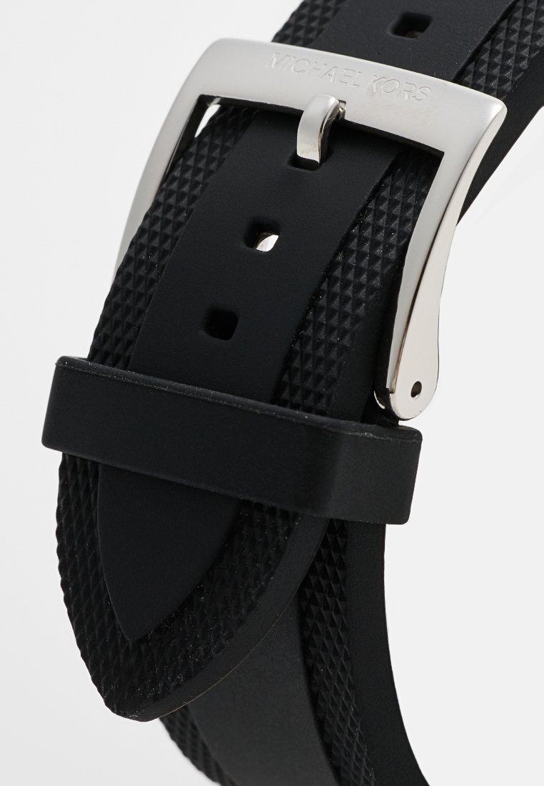 Schwarzes Gummiband mit strukturiertem Oberflächenfinish, silberner Metallschnalle und Michael Kors Branding. Fünf Einstelllöcher für die Passform.