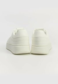 Białe sneakersy z gładką syntetyczną cholewką, okrągłym noskiem i grubą platformą. Posiadają wyściółkę w okolicy kostki oraz teksturowaną podeszwę.