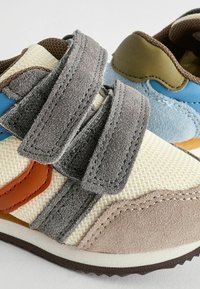 Kinder sneakers met mesh en suede panelen in beige, blauw en bruin, met grijze klittenbandsluitingen en rubberen zolen voor grip.