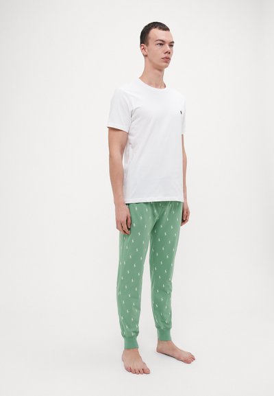 T-shirt en coton blanc associé à un pantalon de pyjama vert avec un motif de logo répété. Les pantalons ont des poignets et une taille élastiques.