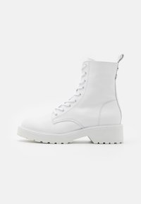 Weiße Leder-Stiefeletten mit runder Zehenpartie, Schnürung vorne und dicker weißer Sohle. Sie haben einen leichten Absatz und eine Schlaufe an der Rückseite.