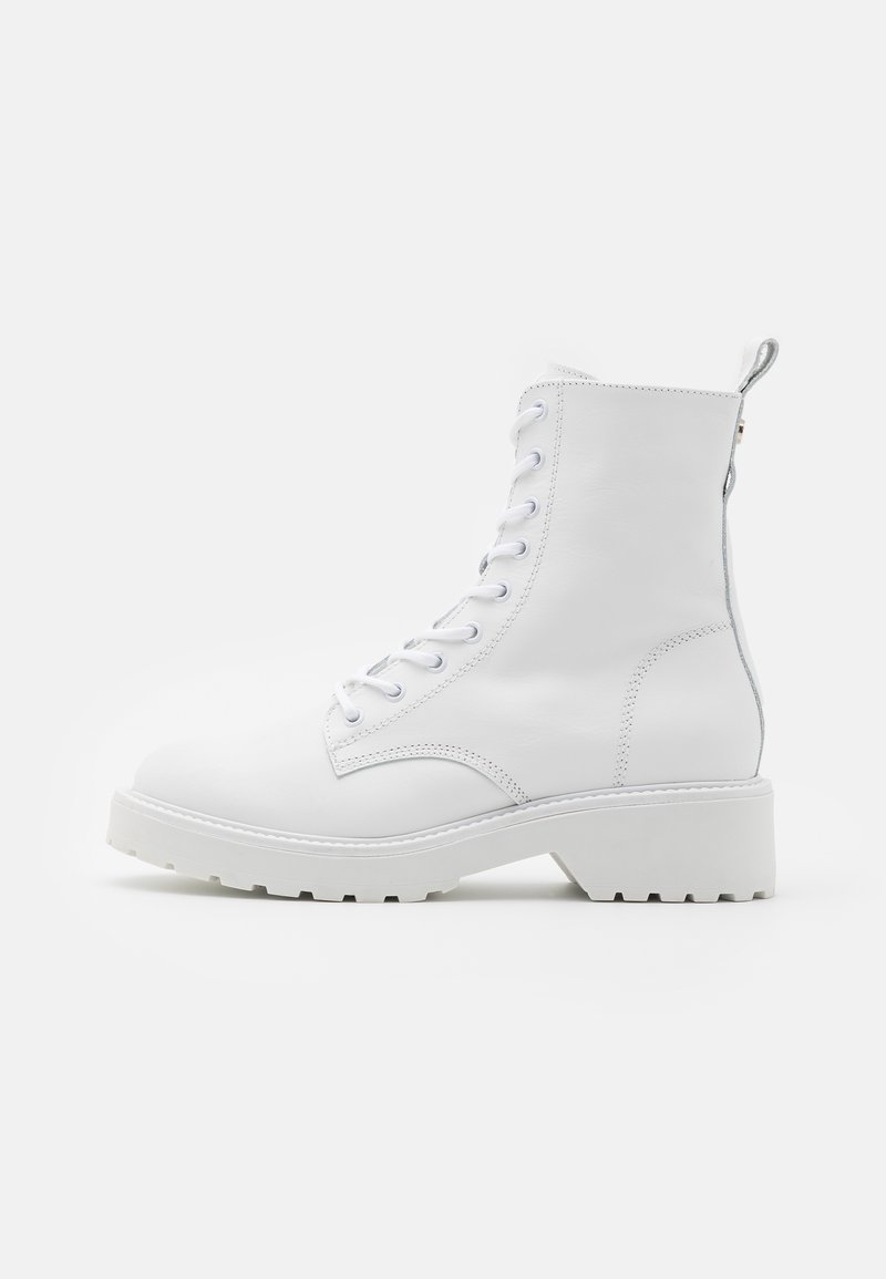 Weiße Leder-Stiefeletten mit runder Zehenpartie, Schnürung vorne und dicker weißer Sohle. Sie haben einen leichten Absatz und eine Schlaufe an der Rückseite.