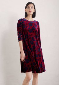 Sammetklänning i djup röd med blå blommönster, med trekvartsärmar och avslappnad passform, som når ovanför knäet.