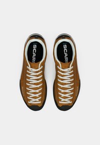 Kastanjasuede sneakers valgete paeltega, musta kummitaldiga ja logoga külgedel. Tekstiilvooder ja minimalistik disain.