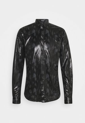 Musta pitkähiha napillinen paita, jossa on kiiltävä käärmeenahkamainen pinta ja hillitty leopardikuvio, yksinkertaisella vaalealla taustalla.