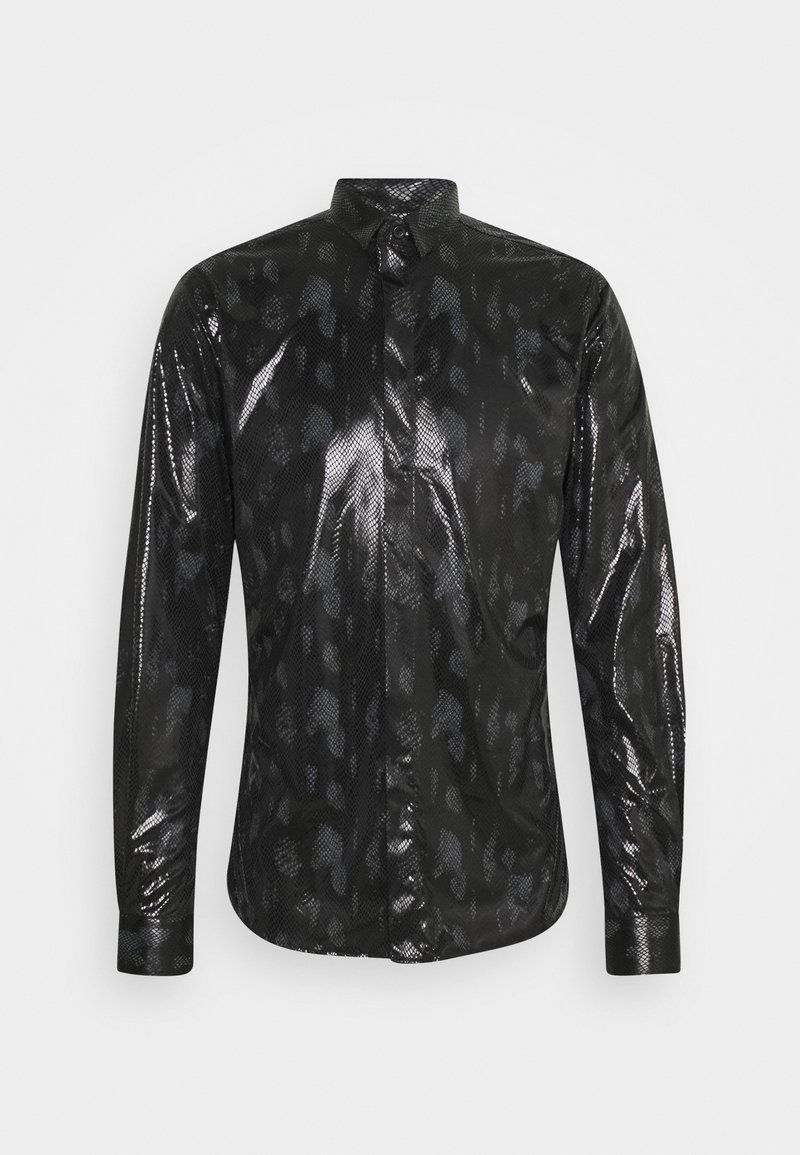 Chemise noire à manches longues avec boutons, texture brillante effet peau de serpent et motif léopard subtil sur un fond clair uni.