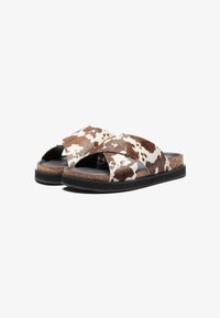 Sandales en cuir de vache marron et blanc avec des brides croisées, semelle en liège et semelle en caoutchouc noir. Texture lisse avec un motif naturel.