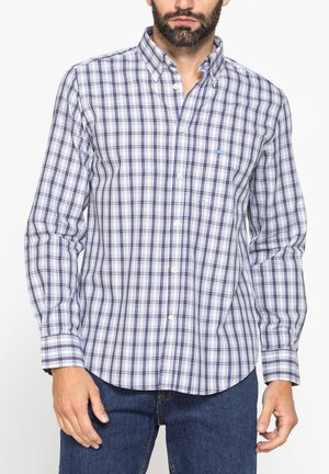 Uomo che indossa una camicia a quadri blu e bianca con collo e jeans blu, mostrato dal petto ai fianchi.
