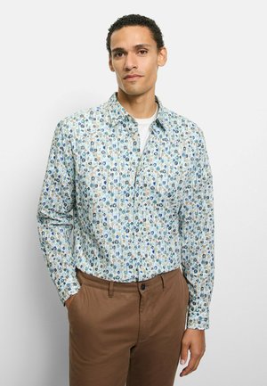 Hellblaues Hemd mit Knöpfen und floralem Muster in Grün, Blau und Beige. Lange Ärmel und ein klassischer Kragen. Kombiniert mit braunen Hosen.