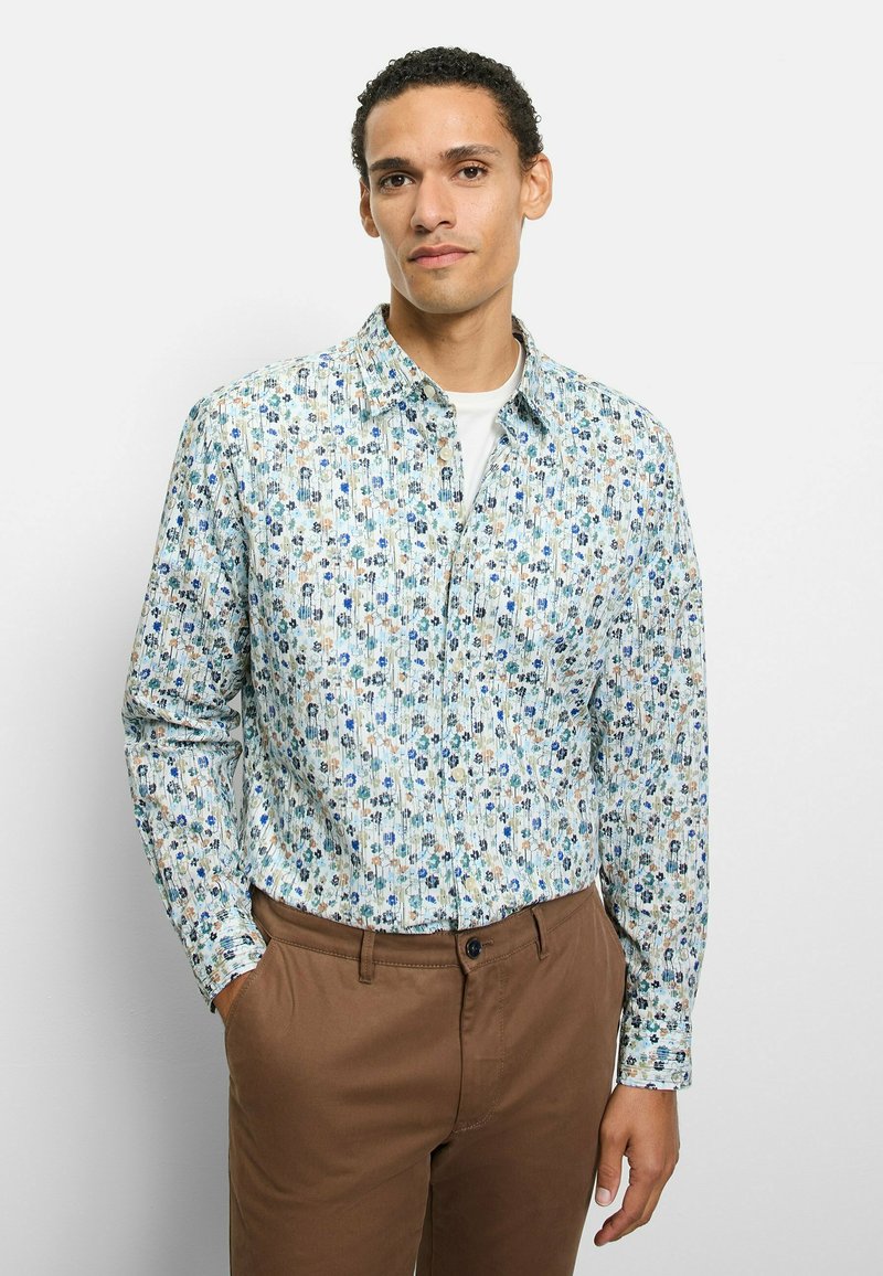 Hellblaues Hemd mit Knöpfen und floralem Muster in Grün, Blau und Beige. Lange Ärmel und ein klassischer Kragen. Kombiniert mit braunen Hosen.