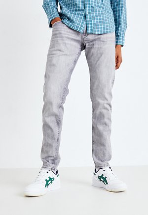 Jeans de denim gris con ajuste slim, que presentan un ligero desgastado y patrones de desgaste, combinados con zapatillas blancas con acentos verdes.