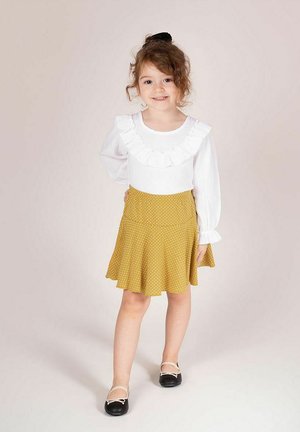 Biała bluzka z falbanianym kołnierzykiem, żółta spódnica w kropki i czarne baleriny. Strój charakteryzuje się miękkimi teksturami i rozkloszowanym kształtem spódnicy.