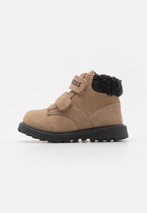 Bottine pour tout-petit en daim beige avec col en polaire noire, double bande Velcro et semelle en caoutchouc noire sur fond blanc.