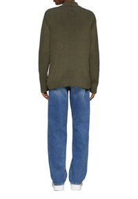 Dunkelgrüner, gerippter Strickpullover kombiniert mit hellblauen, entspannten Jeans und weißen Sneakers, von hinten betrachtet.