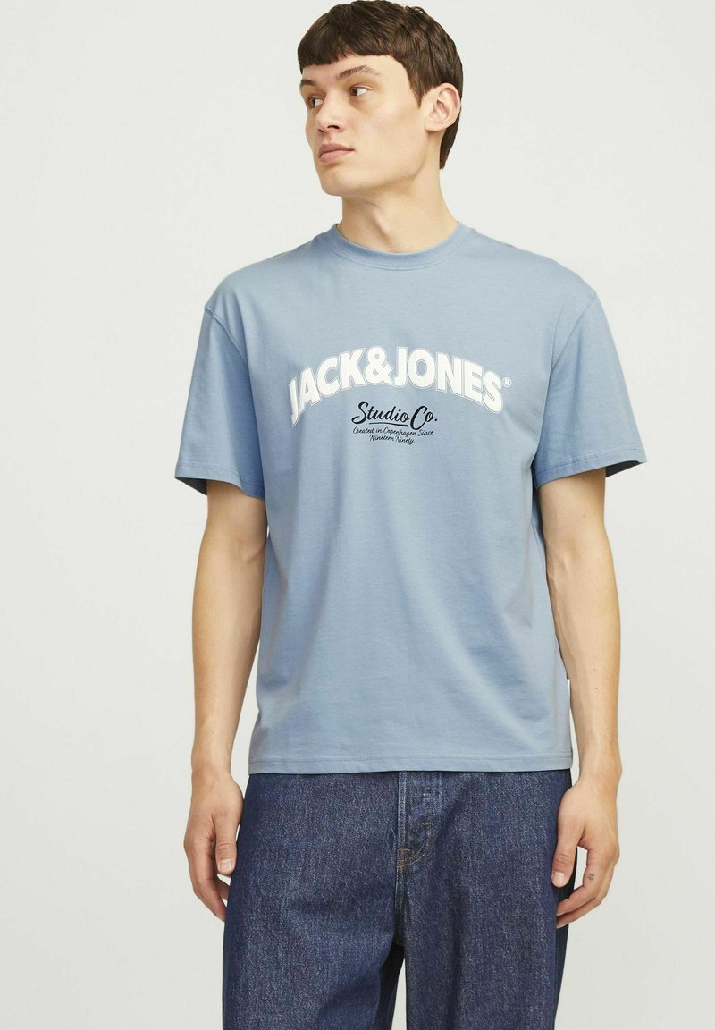 Camiseta de algodón azul claro de manga corta, con el texto en blanco "JACK&JONES" en negrita y un logotipo negro más pequeño debajo. Textura suave.