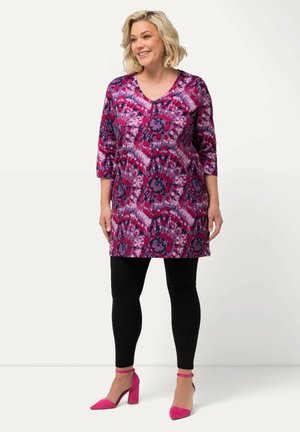 Tunik ungu cerah dengan pola floral, lengan ¾, dan leher V, dipadukan dengan legging hitam dan sepatu hak tinggi berwarna merah jambu.