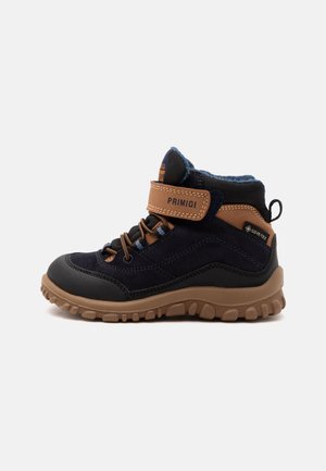 Botte d'hiver enfant bleu foncé et marron avec une sangle marquée Primigi, semelle robuste et tissu Gore-Tex pour une protection imperméable.