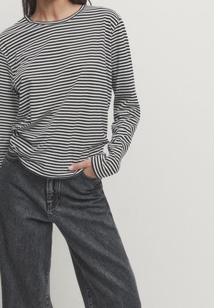 Woman wearing a black and white long-sleeve striped shirt tucked into high-waisted black denim jeans with one hand in pocket.