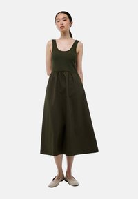 Robe vert olive foncé avec un bodice en haut ajusté et une jupe fluide et froncée. Fabriquée en tissu léger, arrivant au milieu du mollet.