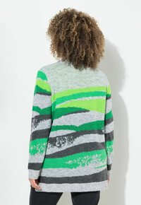 Grå stickad cardigan med gröna och svarta vågmönster, med ribbad nederkant och ärmslut. Mellanlång med en avslappnad passform och mjuk textur.