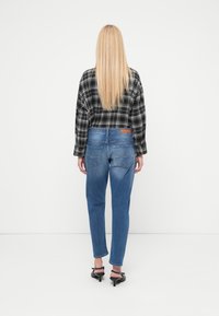 Vista trasera de una persona que lleva una camisa a cuadros en blanco y negro, jeans de mezclilla azul con una etiqueta marrón en la cintura y tacones negros.