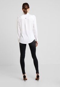 Weißes Langarmhemd mit Rückenpasse, kombiniert mit schwarzen Skinny-Jeans und schwarzen High-Heel-Sandalen, von hinten betrachtet.