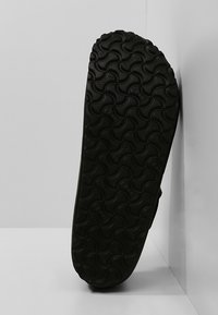 Fekete gumi cipőtalp hullámos mintázattal, kerek barázdákkal és texturált felülettel. Függőlegesen áll egy semleges háttér előtt.