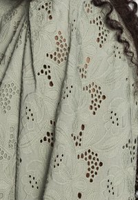 Ljusgrön broderad tävling med blommönster och utskurna mönster. Har en mjuk textur och känsliga detaljer, vilket skapar en lagerlook.