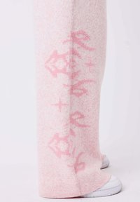 Soft pink wide pants with darker pink patterns worn over white sneakers on a light background.
