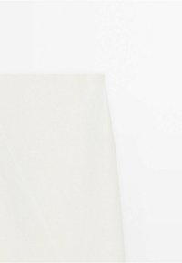 Gros plan d'un tissu uni beige clair plié formant un pli diagonal subtil et net sur fond blanc.
