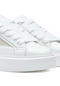 Białe skórzane sneakersy z grubymi, teksturowanymi sznurowadłami, gładką osłoną palców i subtelnymi siateczkowymi panelami po bokach. Posiadają masywną białą podeszwę.