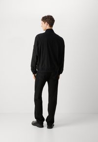 Černá bomber bunda s stojáčkem, elastickými manžetami a spodním lemem; na levém rukávu je nášivka. Vytvořeno v kombinaci s černými džíny a botami.