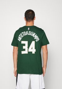 Muž v zeleném dresu Milwaukee Bucks s nápisem "Antetokounmpo" a číslem 34, otočený zády, v bílých basketbalových šortkách.
