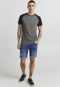Una camiseta raglán gris y negra hecha de tela suave, combinada con unos pantalones cortos de mezclilla con puños enrollados y detalles desgastados, llevados con zapatillas negras.