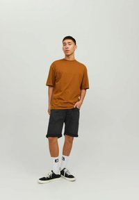 Tricou din bumbac brown, cu mânecă scurtă și guler rotund, asortat cu pantaloni scurți din denim negri. Purtați cu șosete albe și teniși negri.