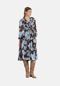 Vestido floral en colores azul y marrón, con cuello con volantes, falda de capas y mangas largas, combinado con botas beige hasta la rodilla.
