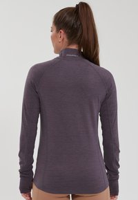 Long-sleeve, purple athletic top made of lightweight, textured fabric with a high collar and thumbholes at the cuffs. Seamless design accents.