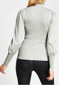 Ljusgrå ribbad tröja med puffärmar och hög krage. Har en strukturerad yta och en figurnära silhuett, visad bakifrån.